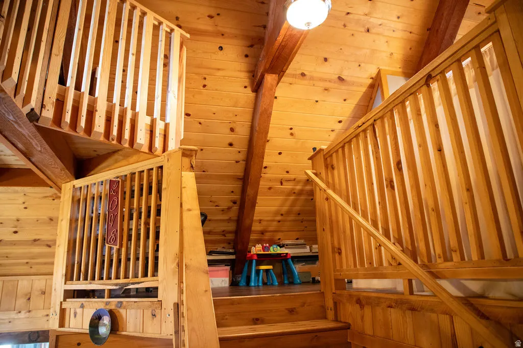 Wood-paneled interior featuring an open-tread staircase with wood balusters, exposed wood beams, a vaulted wood-clad ceiling, and an overhead light fixture
