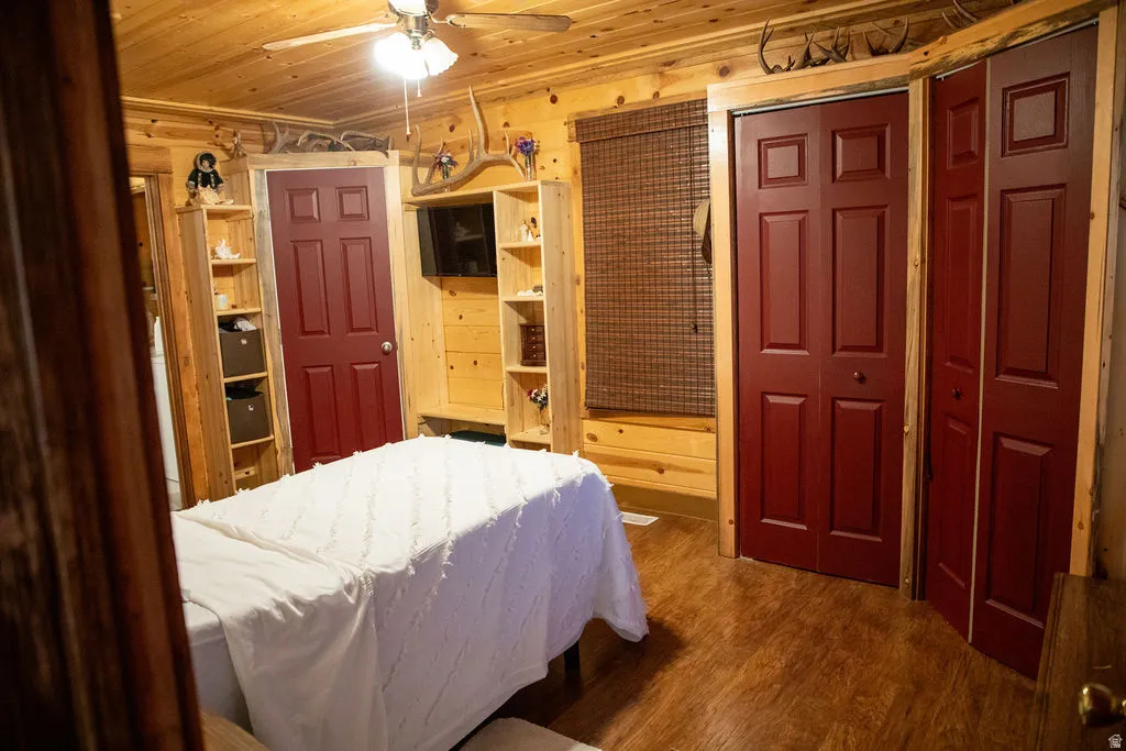 Wood-paneled room featuring wood-finish flooring, a ceiling fan with integrated lighting, and multiple recessed shelving units