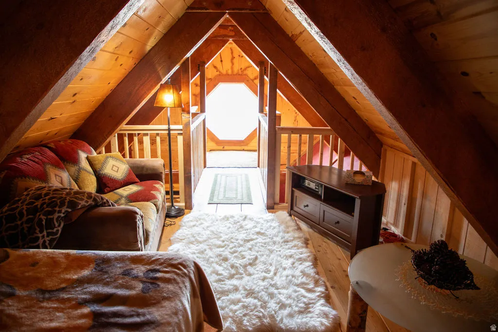 Wood-finish flooring throughout an attic space featuring exposed wood beams, wood-paneled walls, and a prominent octagonal window at the far end