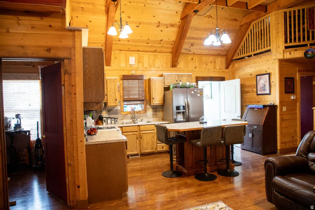Kitchen featuring wood-finish flooring, natural wood paneling, wood beam vaulted ceilings, stainless steel appliances, and a central island with bar seating
