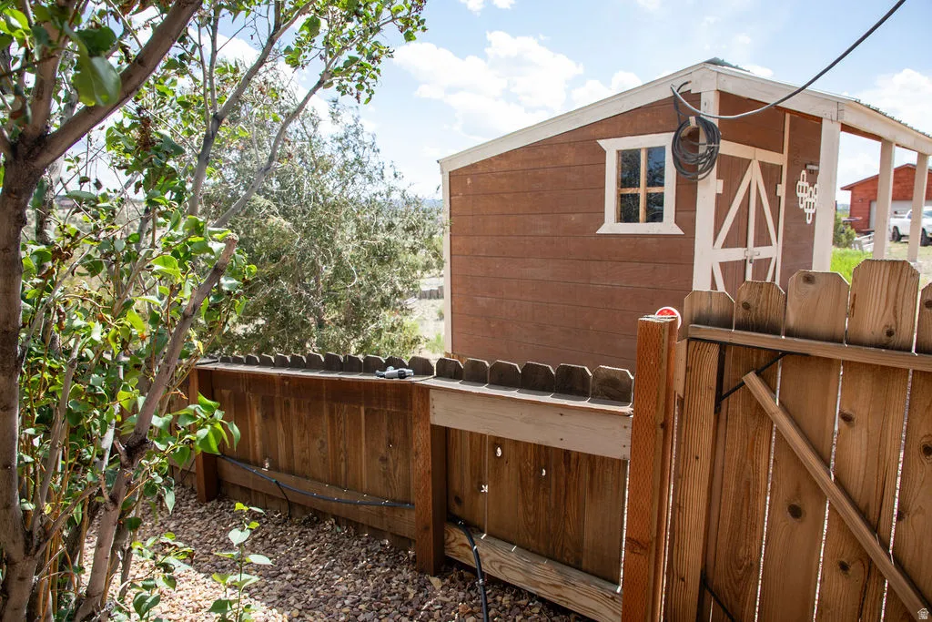 Detached wooden shed featuring a white-trimmed window and barn-style door, set behind a wooden privacy fence with an integrated gate