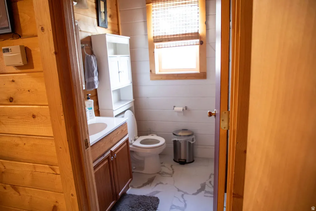 Bathroom featuring a wood-finish vanity with an integrated sink, a white storage cabinet, a toilet, a window with a woven shade, and white shiplap walls