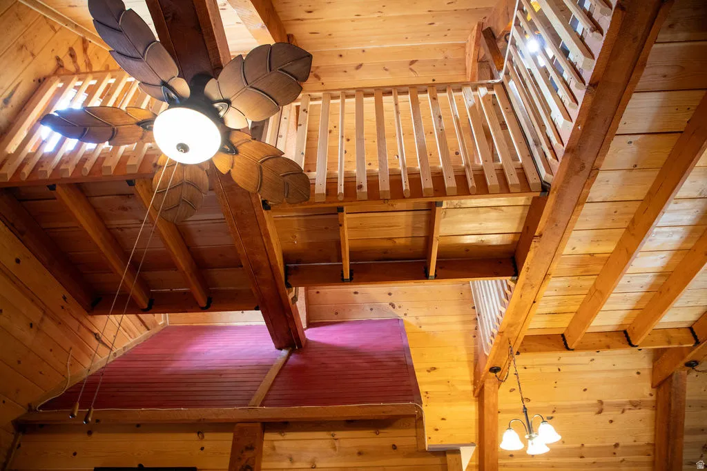 Expansive wood-paneled interior featuring a decorative ceiling fan with leaf-shaped blades, an upper-level wood railing, and exposed wood beams