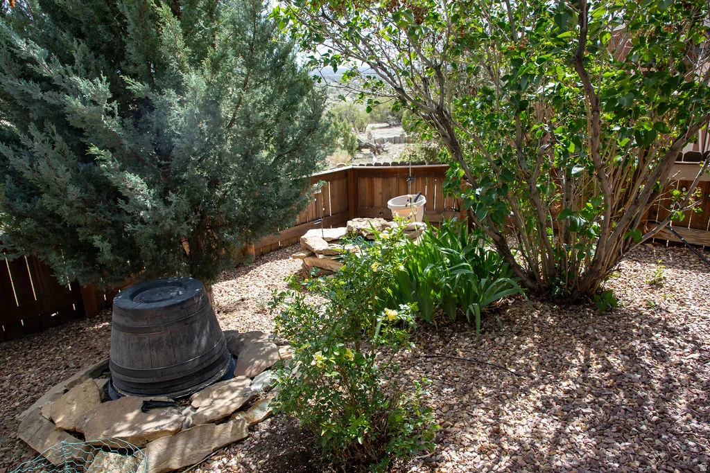 Landscaped backyard featuring a mature evergreen tree, established shrubs, a wooden privacy fence, a decorative barrel feature, and a gravel ground cover