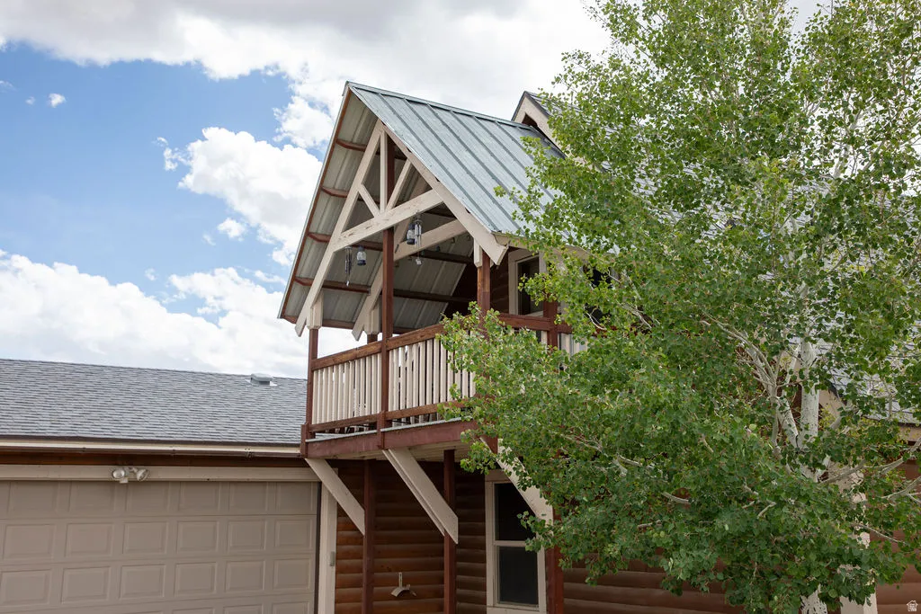 Balcony with exposed timber framing and metal roofing, complemented by log siding and a light-colored garage door