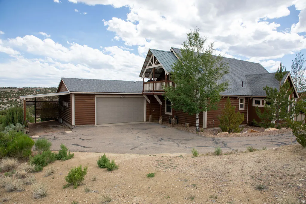 Wood-sided exterior featuring an attached two-car garage, covered carport, second-story balcony, and a multi-pitch roofline with metal and shingle roofing materials