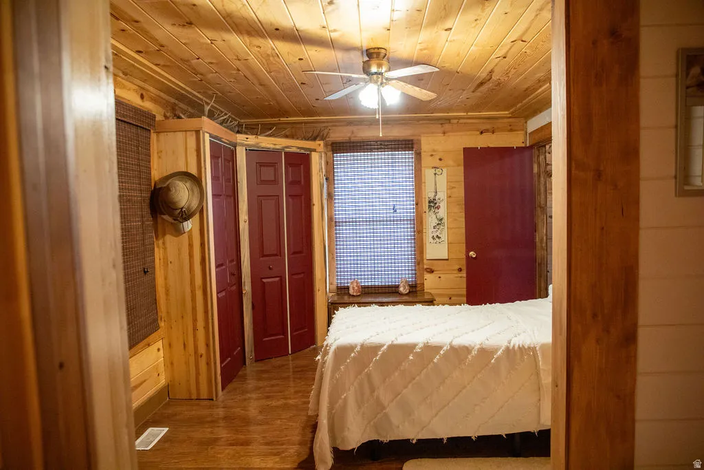 Wood-paneled room featuring a ceiling fan with integrated lighting, wood-finish flooring, and red bi-fold closet doors