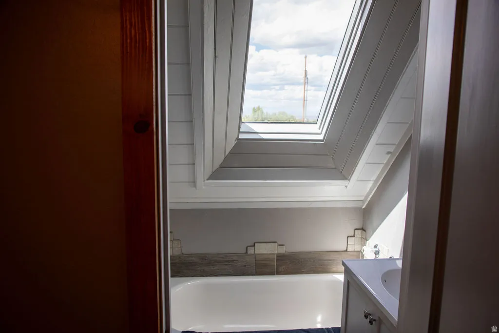White bathtub with a wood-finish tile surround, complemented by a single-sink vanity with white cabinetry and chrome hardware