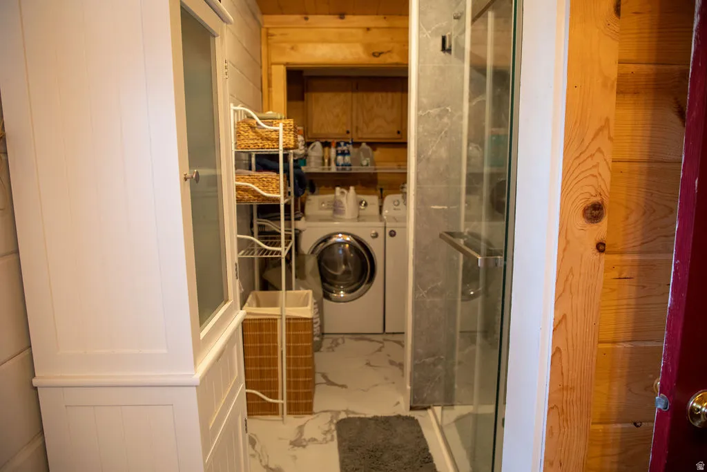 Compact laundry area featuring a front-loading washer and dryer, marble-look flooring, and a glass-enclosed shower with stone-look tile