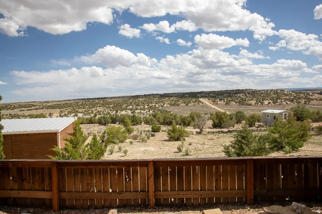 Expansive desert landscape with scattered green vegetation, a wooden privacy fence, and a distant building with a light-colored exterior