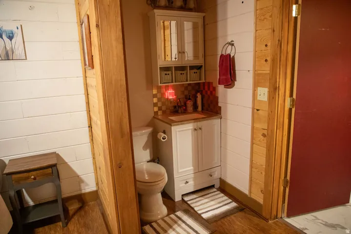 Compact bathroom featuring a white vanity with a brown countertop, a white toilet, and a tiled backsplash