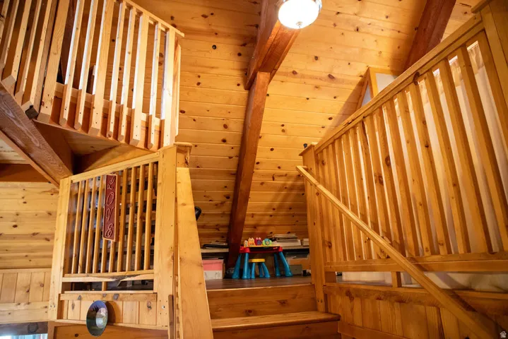 Wood-paneled interior featuring an open-tread staircase with wood balusters, exposed wood beams, a vaulted wood-clad ceiling, and an overhead light fixture