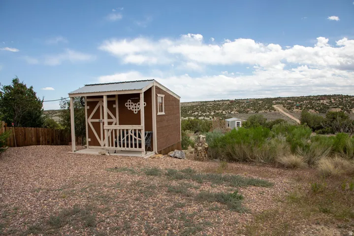 Detached outbuilding featuring a covered porch, white railing, and exterior wall decor