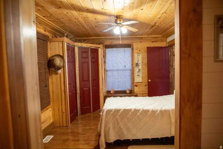 Wood-paneled room featuring a ceiling fan with integrated lighting, wood-finish flooring, and red bi-fold closet doors