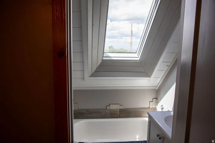 White bathtub with a wood-finish tile surround, complemented by a single-sink vanity with white cabinetry and chrome hardware