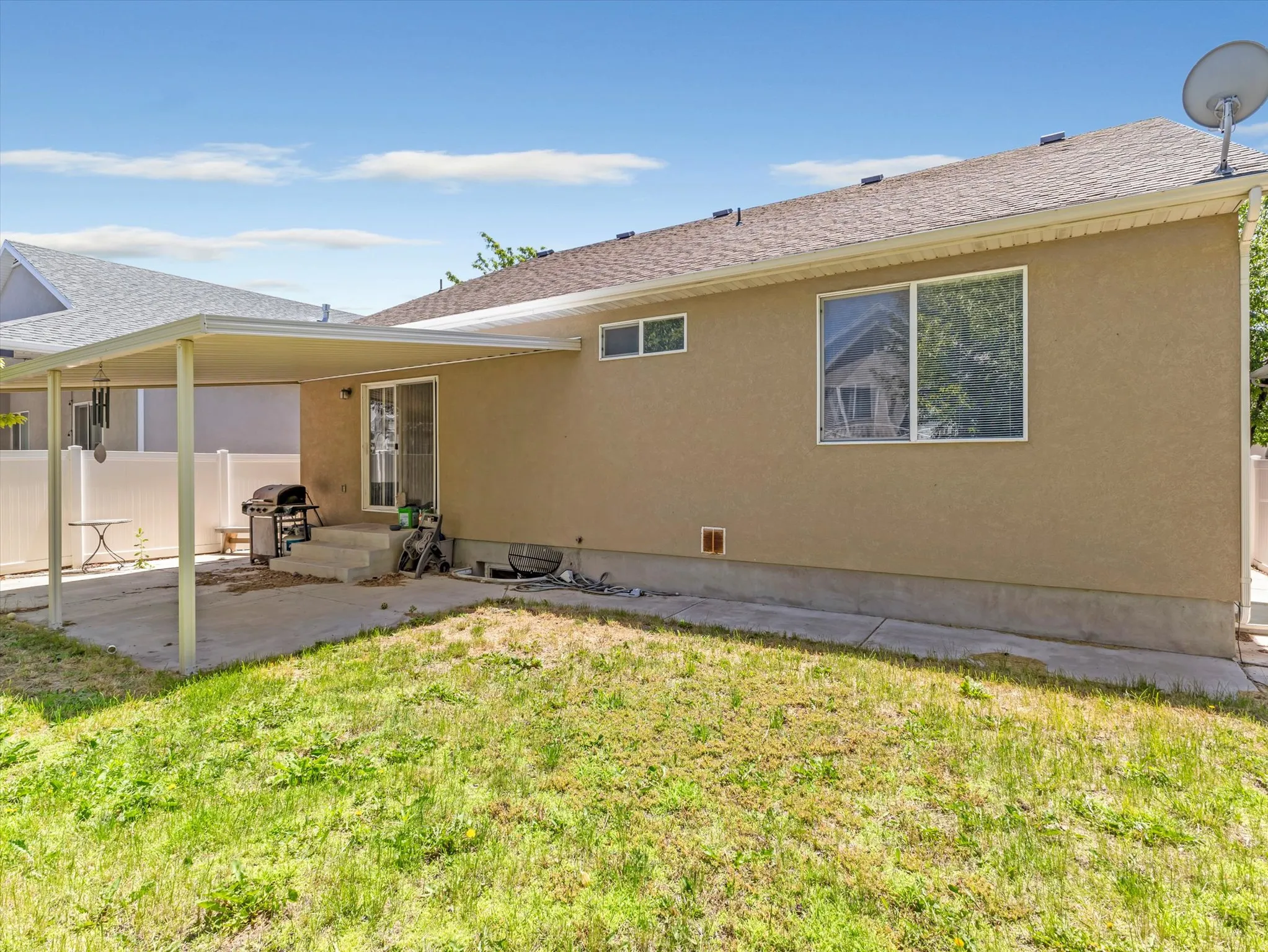 Rear exterior featuring a covered concrete patio, sliding glass door access, stucco siding, and a white privacy fence