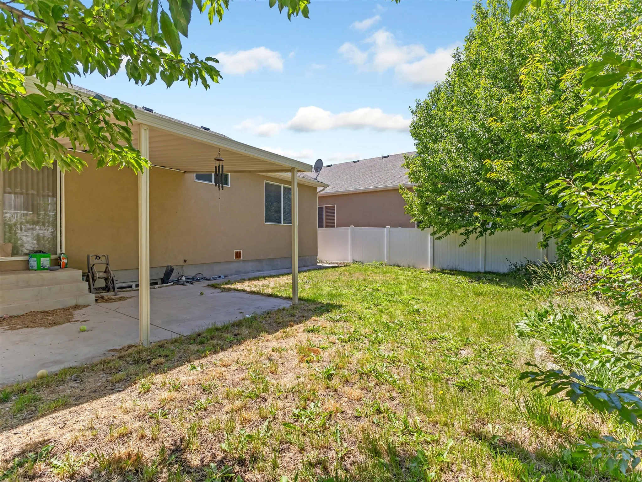 Spacious backyard featuring a covered patio with concrete flooring, stucco exterior, multiple windows, and a privacy fence