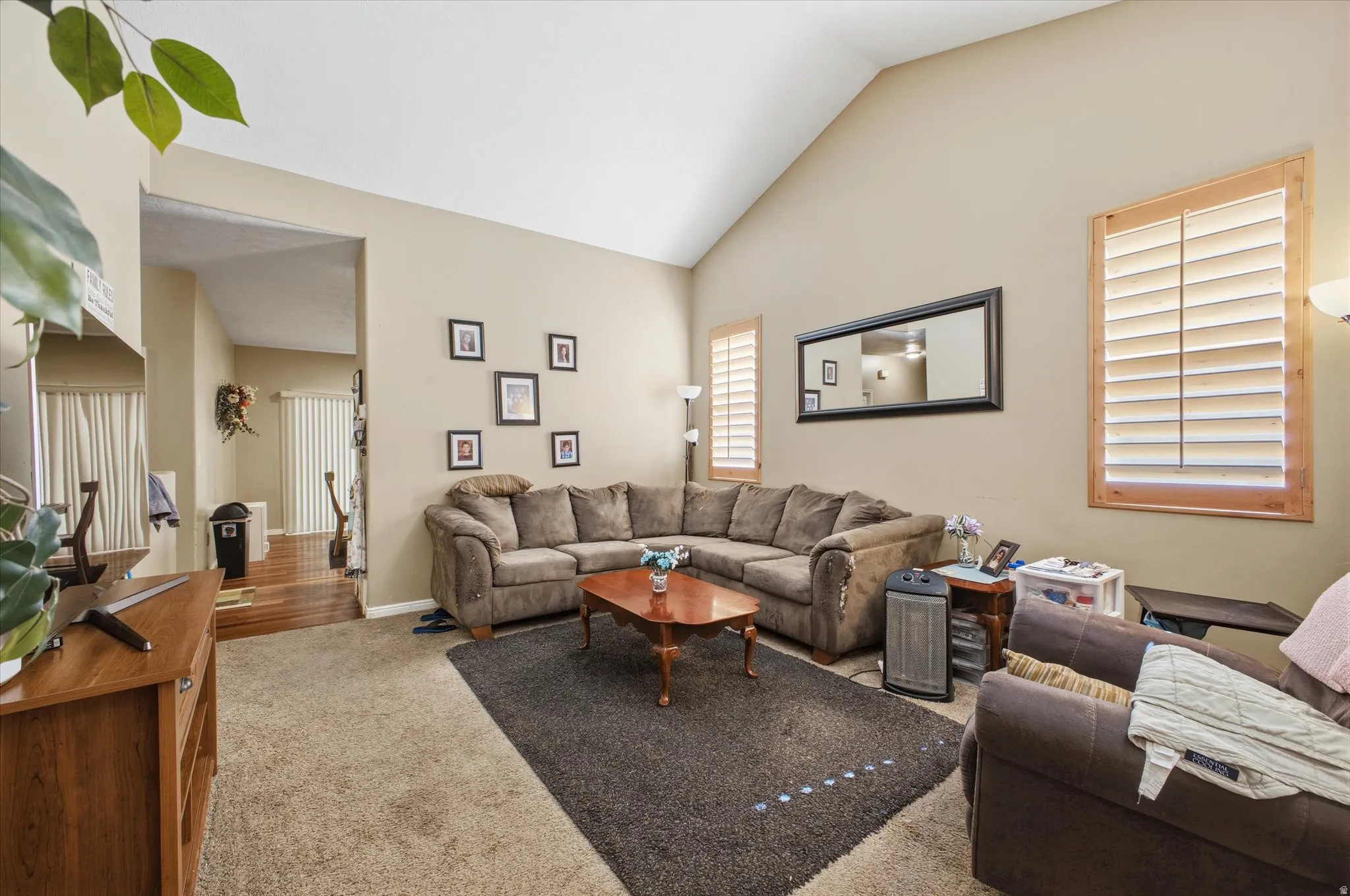 Living area featuring vaulted ceilings, neutral wall tones, and carpet flooring