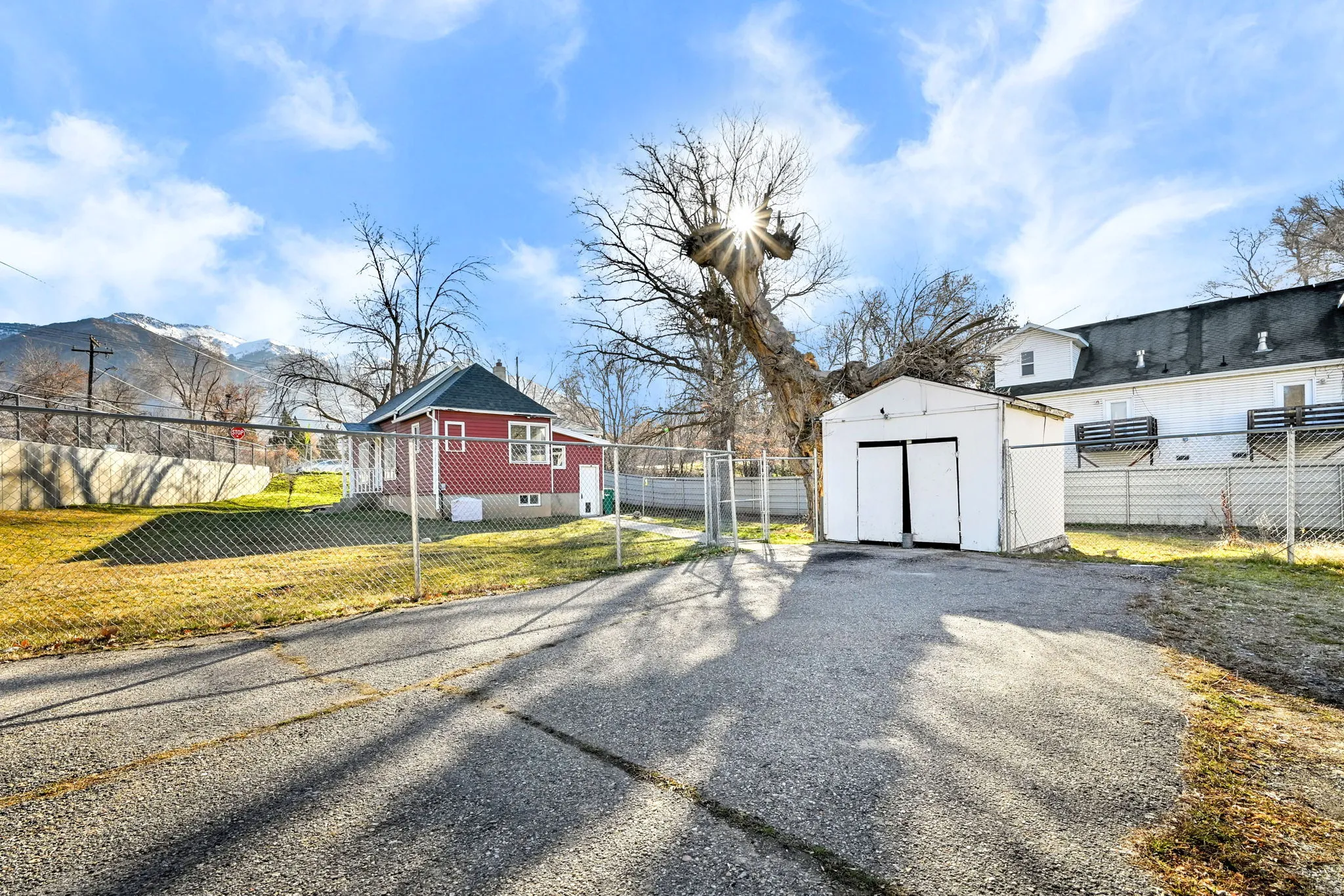 Paved driveway leading to a detached white storage shed with double doors