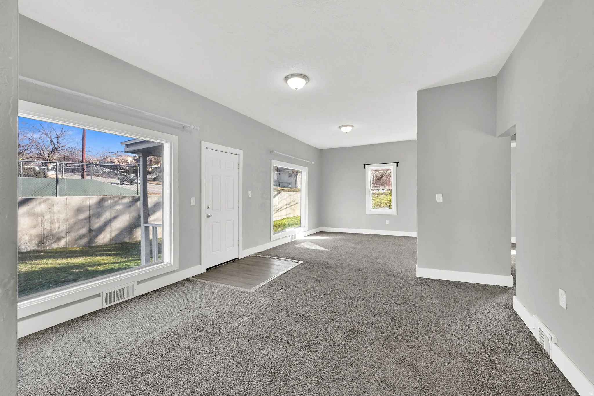 Spacious living area featuring neutral gray wall paint, dark gray carpeting, and white trim