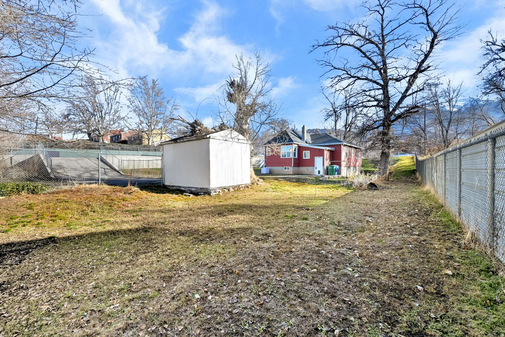Spacious backyard featuring a storage shed, chain-link fencing, and a red-sided structure with a white trim window