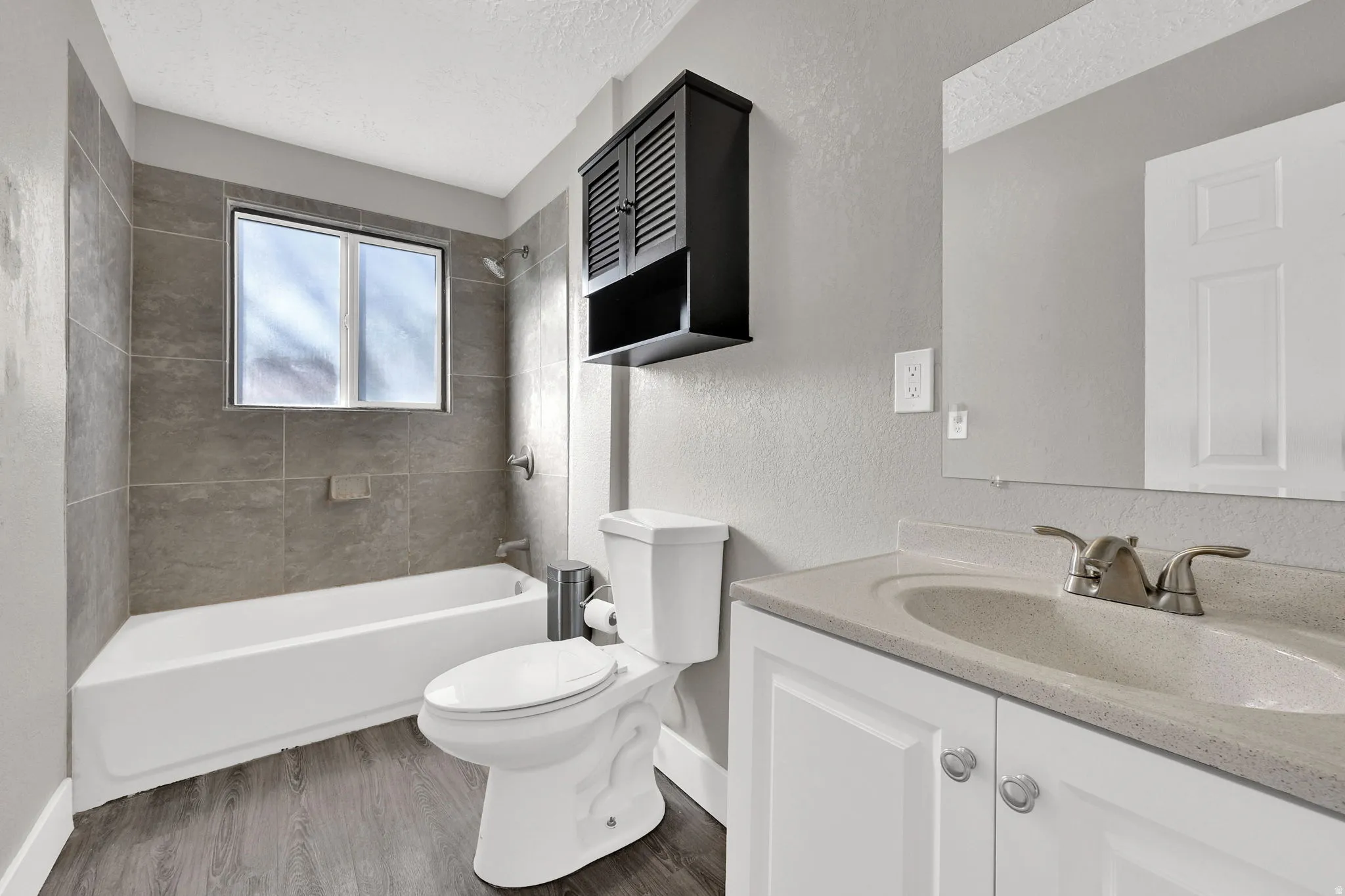Full bathroom featuring a white bathtub with subway tile surround, a single window, a white vanity with integrated sink, and wood-finish flooring