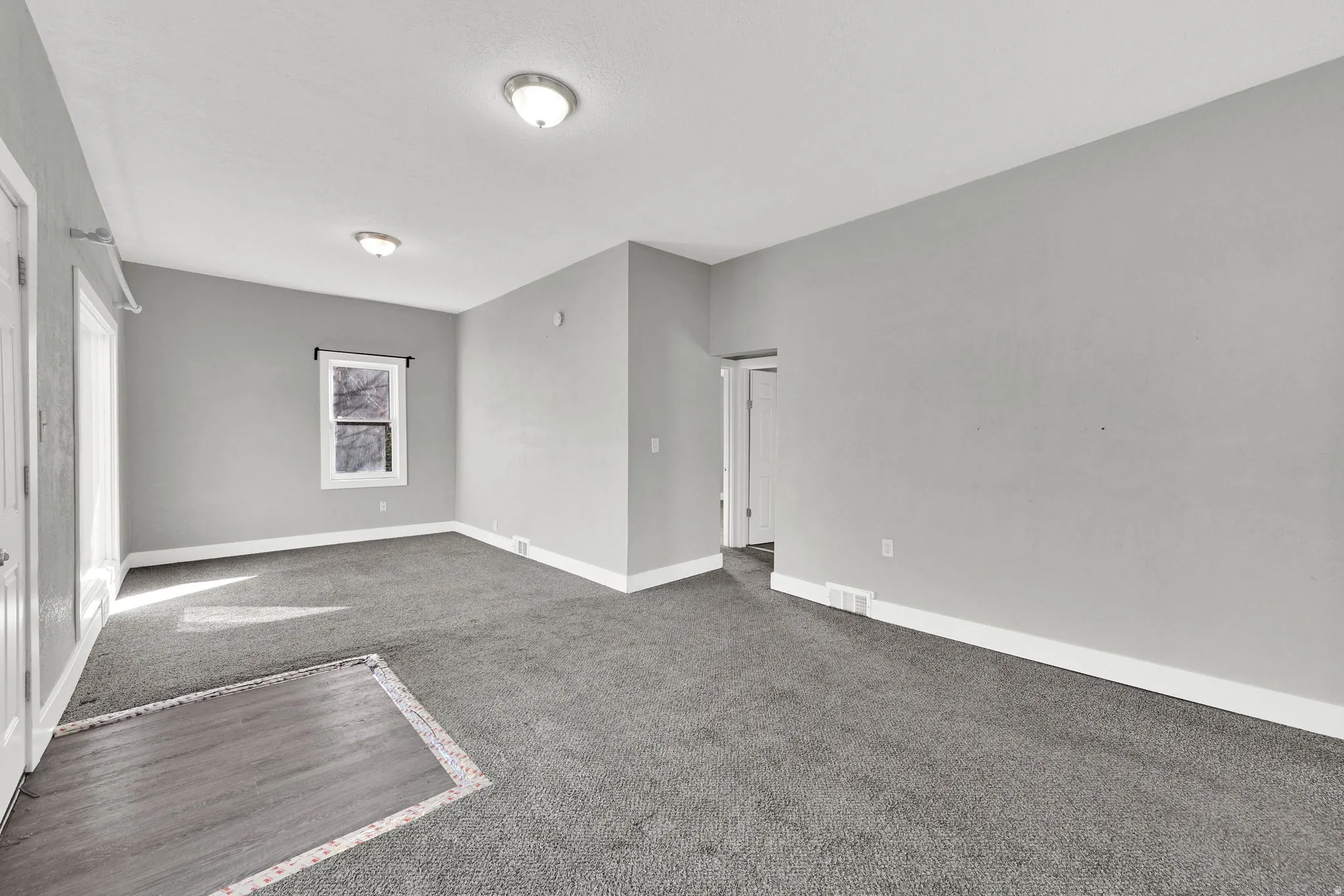 Spacious room with light gray walls, dark gray carpeting, and white baseboards