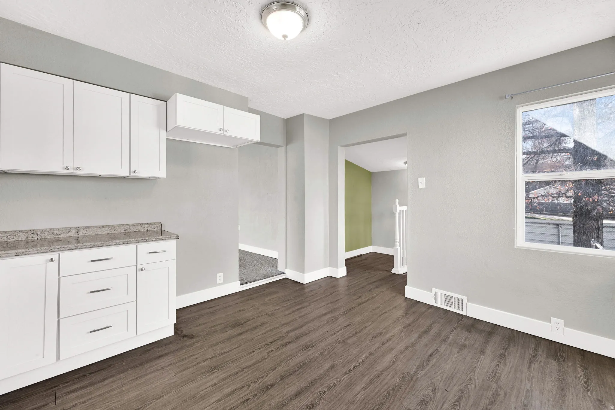 Updated kitchen space featuring white shaker-style cabinetry with chrome pulls, a speckled countertop, and wood-finish flooring