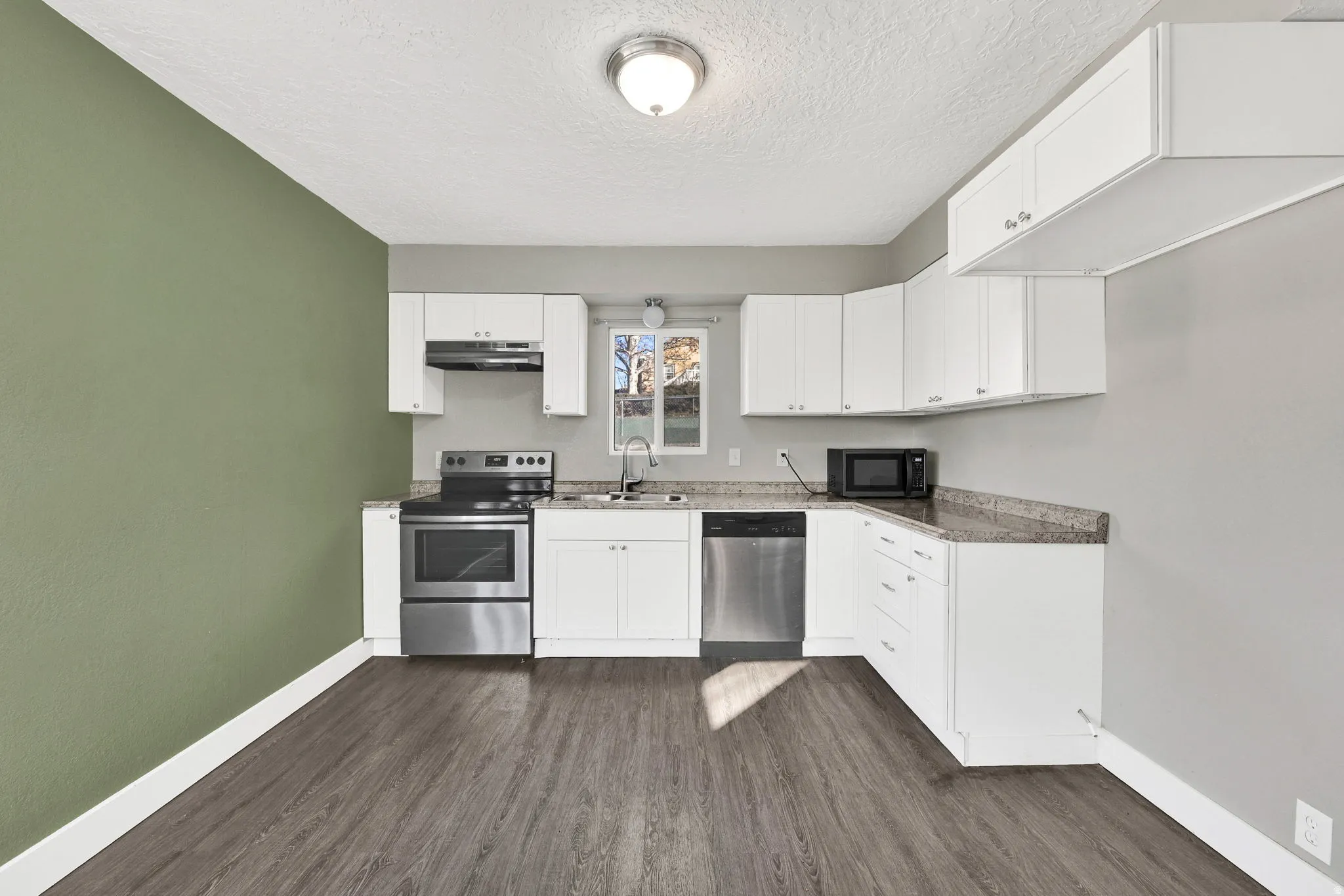 Kitchen featuring wood-finish flooring, white cabinetry, stainless steel appliances, and a window above the sink