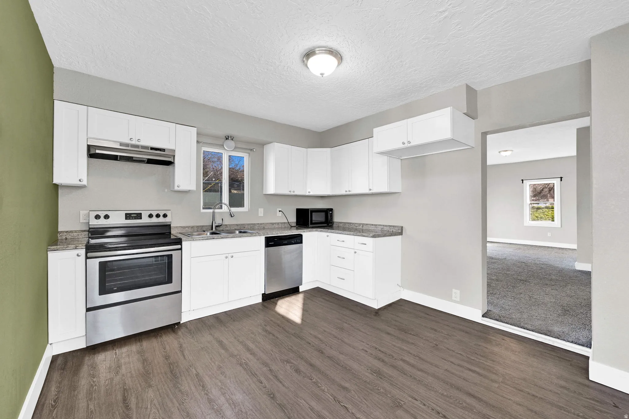 Kitchen featuring white cabinetry, stainless steel appliances, speckled countertops, and wood-finish flooring