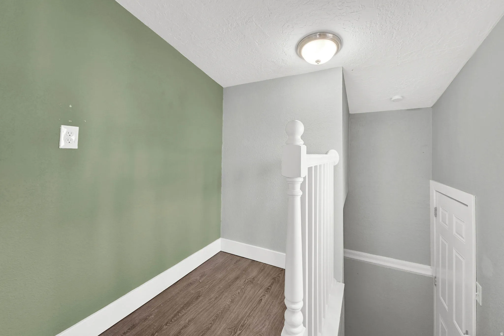 Stairwell landing featuring a white painted balustrade, wood-finish flooring, a contemporary flush mount light fixture, and a paneled interior door
