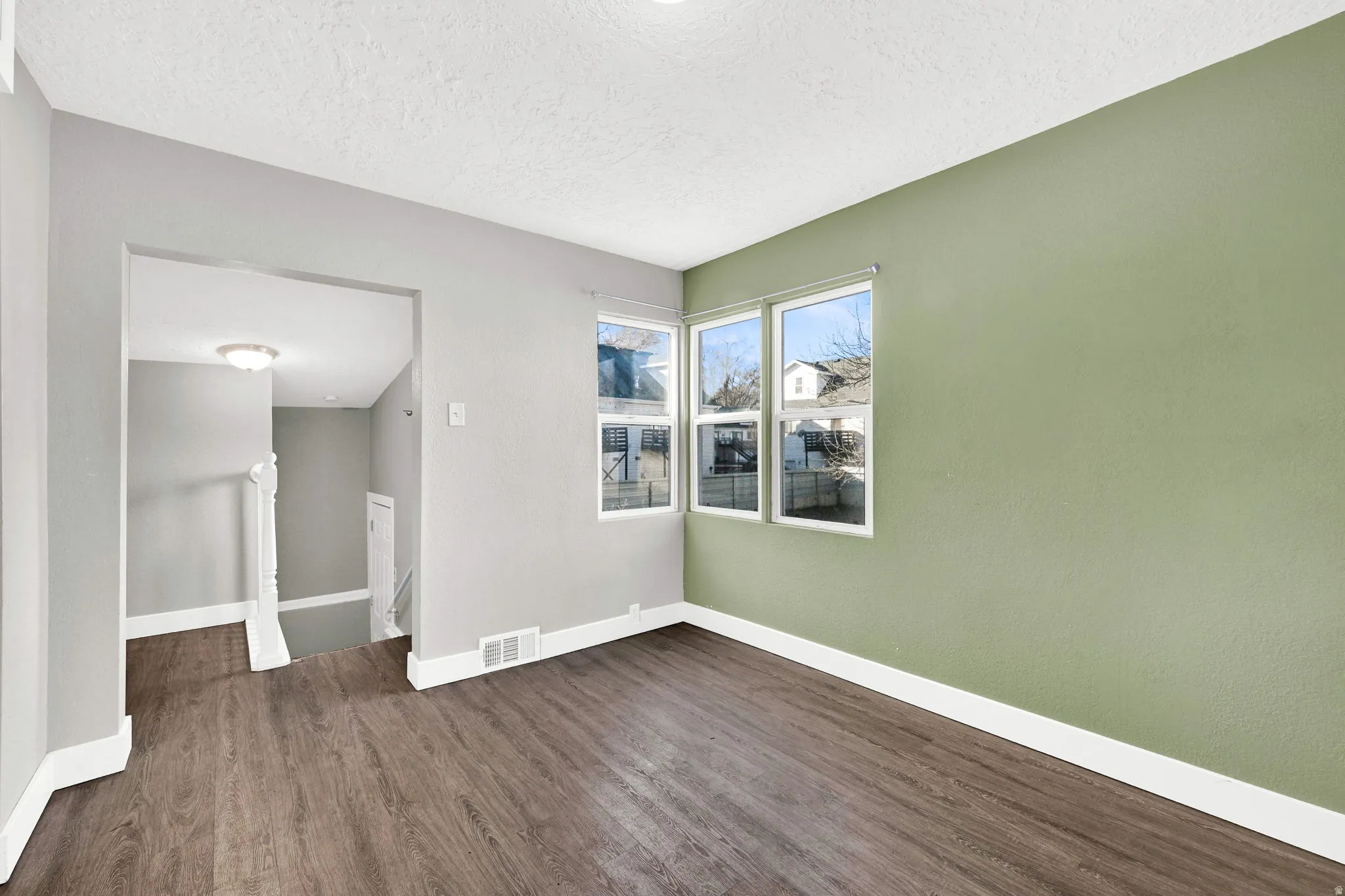 Living area featuring wood-finish flooring, light green accent wall, three pane windows, and an arched doorway leading to a staircase