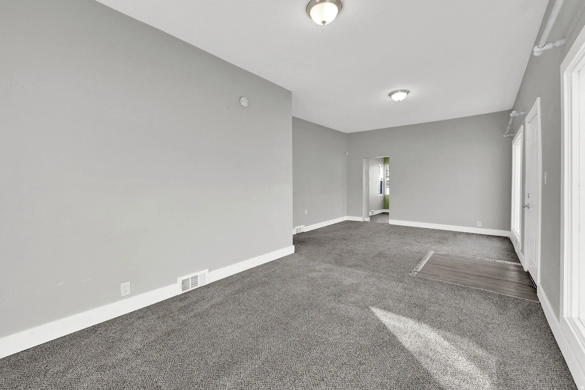 Spacious room featuring gray carpet flooring, light gray wall paint, and white trim