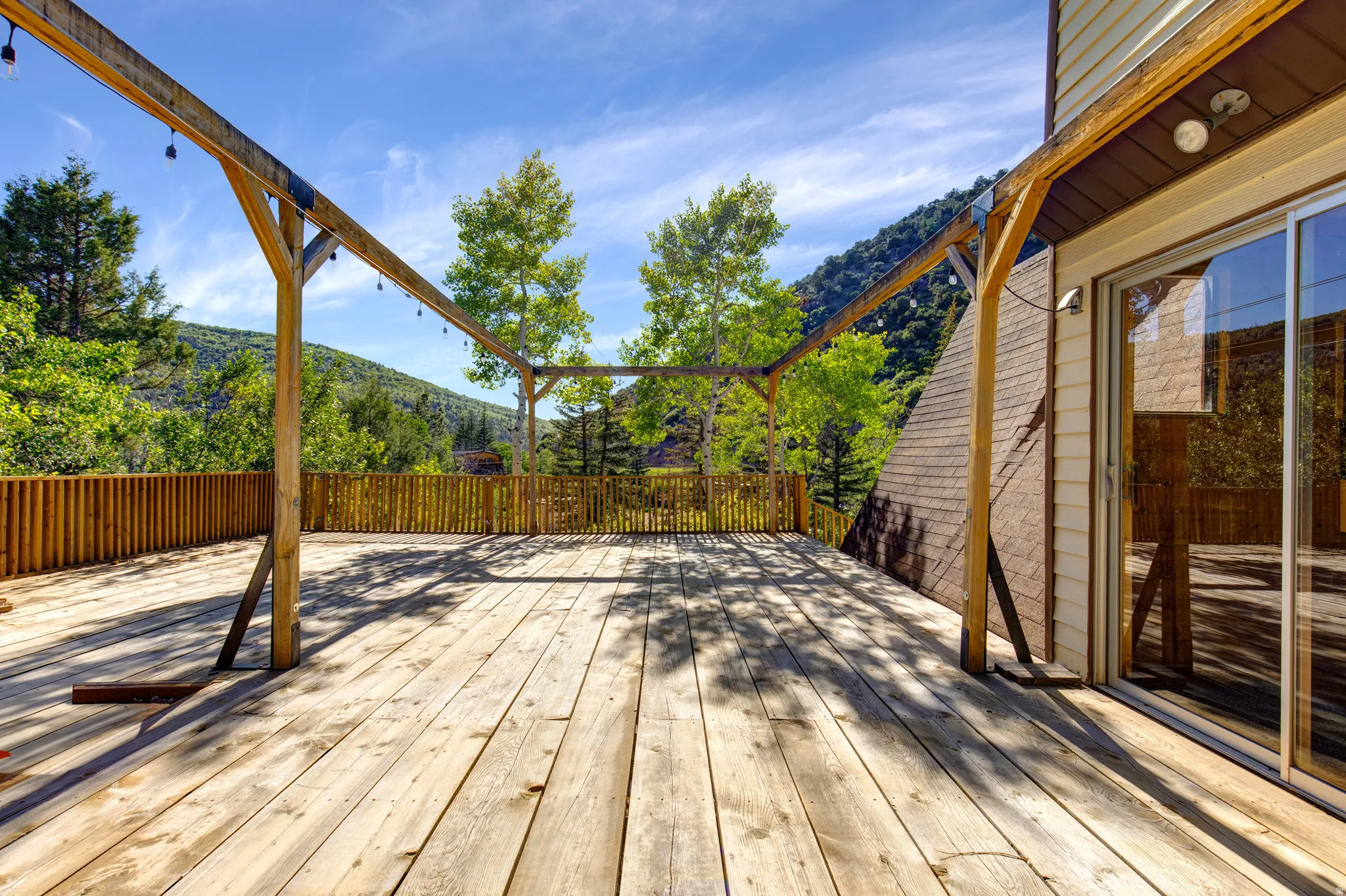 Spacious outdoor wood deck featuring a pergola structure, wood plank railing, and a sliding glass door entry to the interior