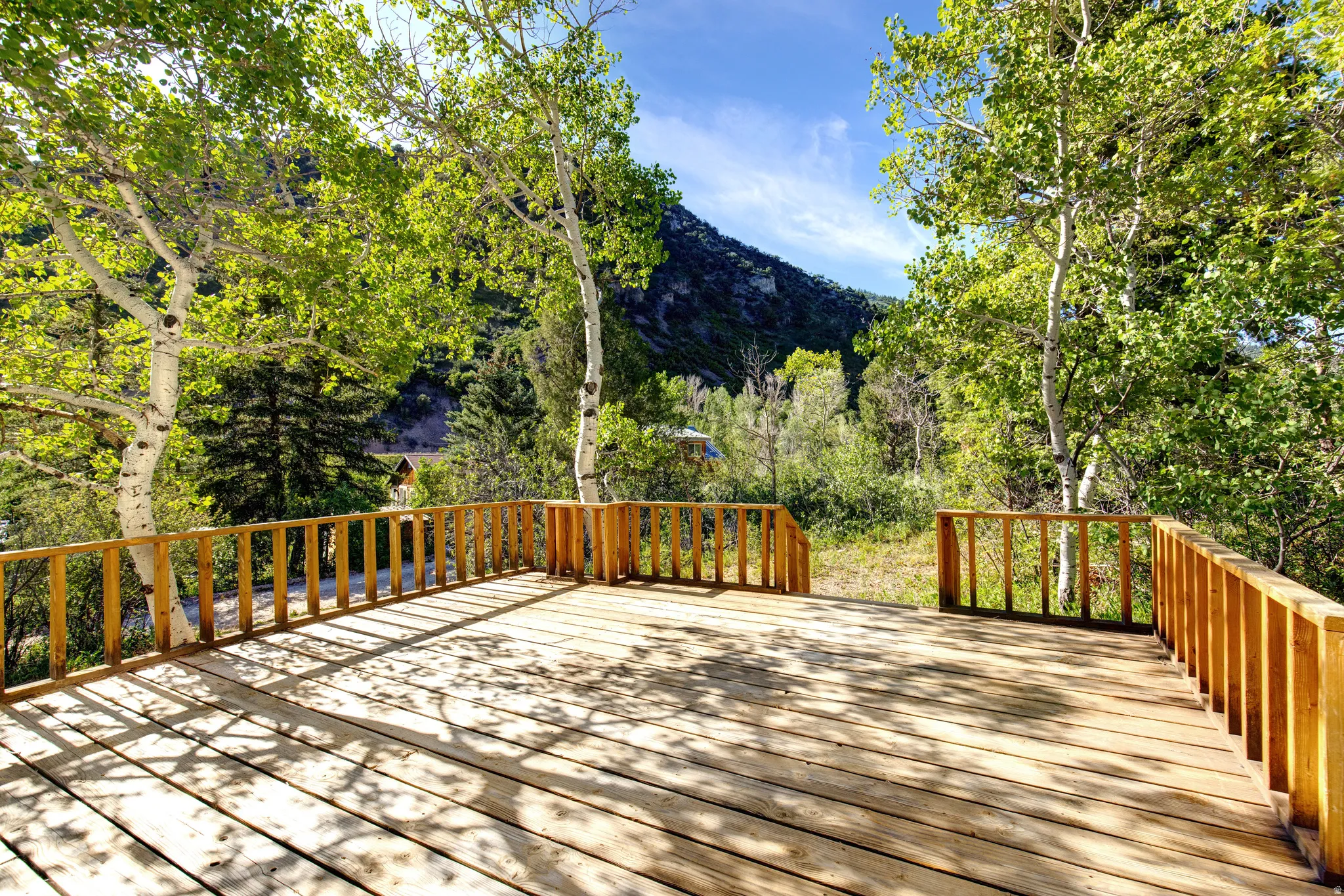 Expansive outdoor deck featuring natural wood decking, sturdy wood railing, and surrounding mature trees