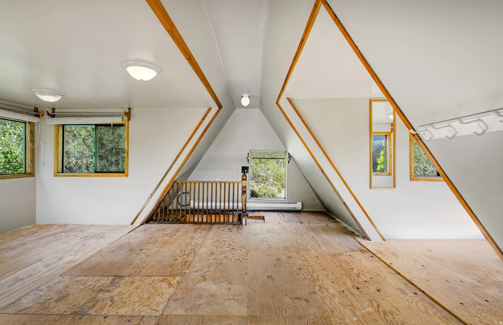 Loft space featuring sloped white walls with exposed wood beams, multiple windows, and light wood flooring
