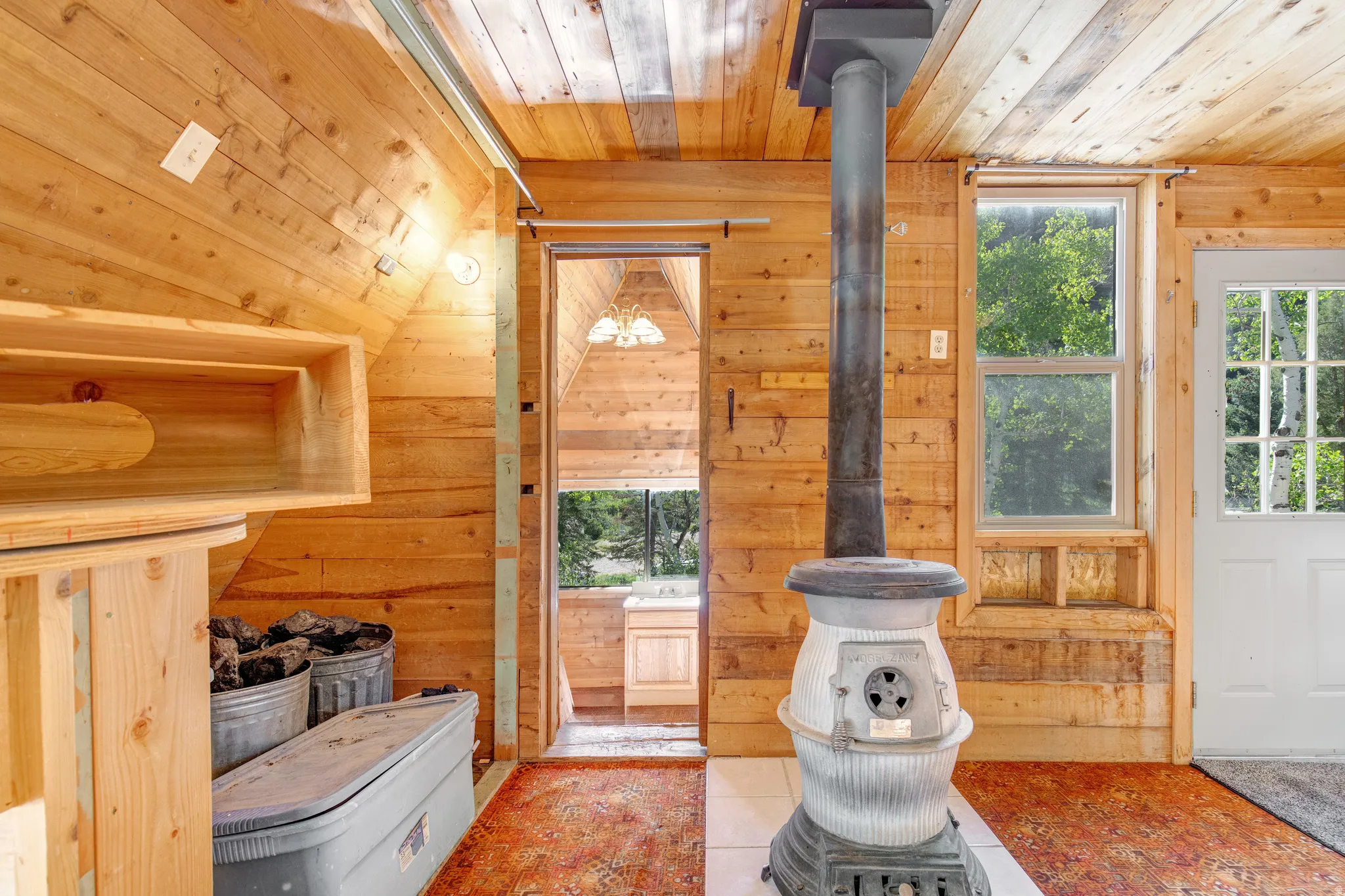 Interior space featuring extensive wood paneling on walls and ceiling, a classic freestanding wood-burning stove, white-framed window, and a white paneled door