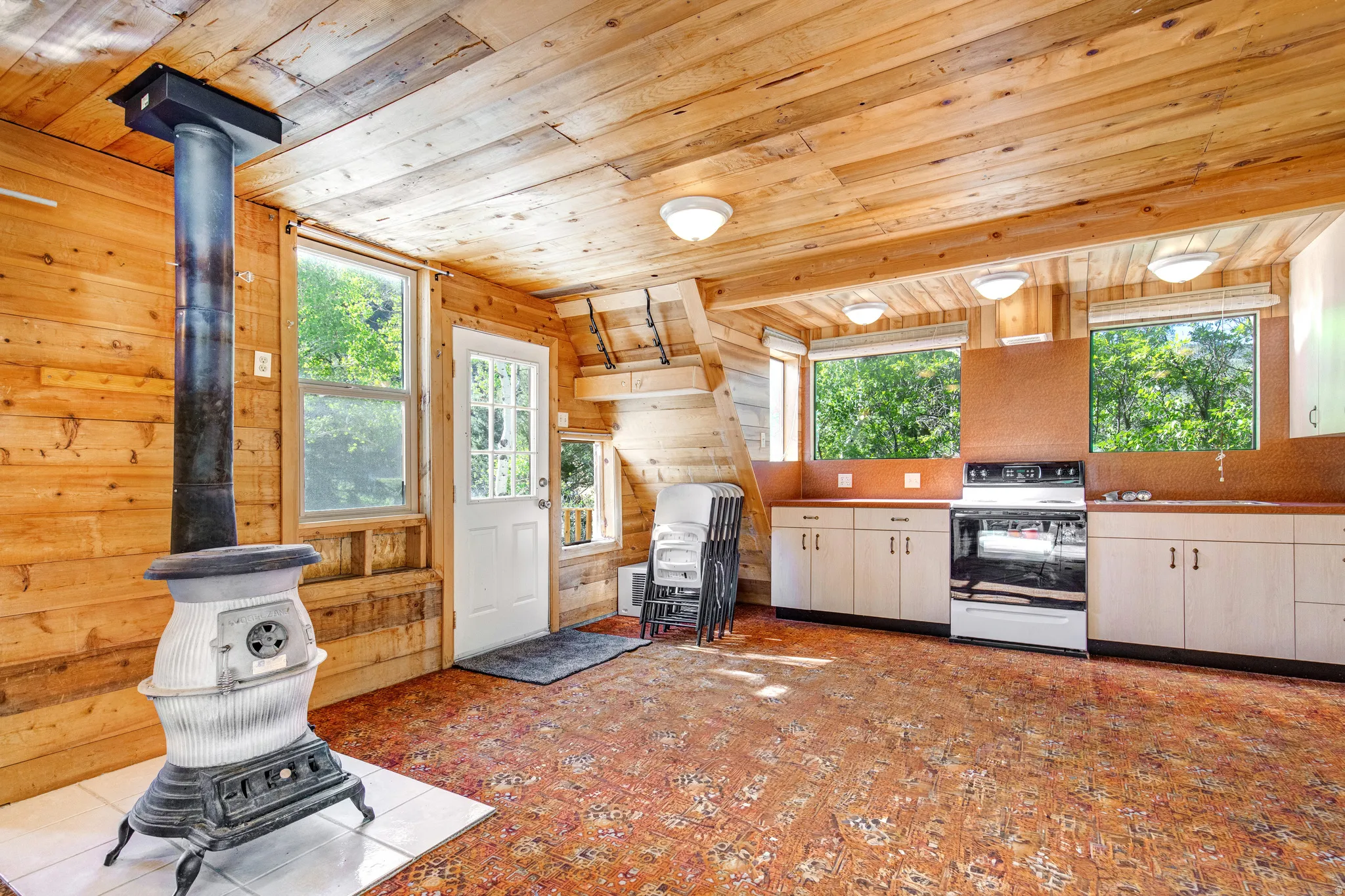 Open-concept space featuring extensive wood-finish wall and ceiling panels, a cast iron stove on a tile hearth, and an integrated kitchen area