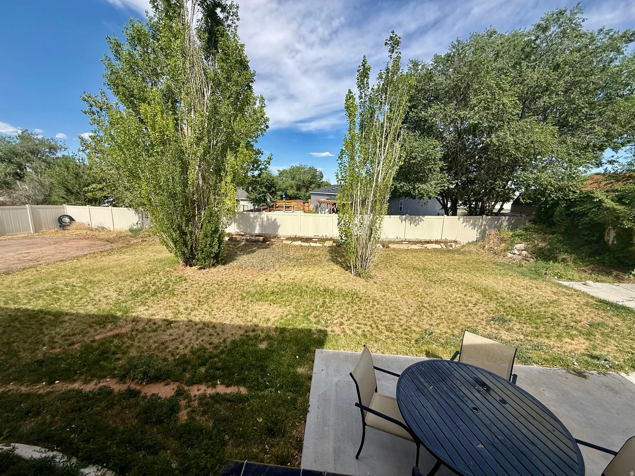 Expansive backyard featuring mature trees, a concrete patio, and perimeter fencing
