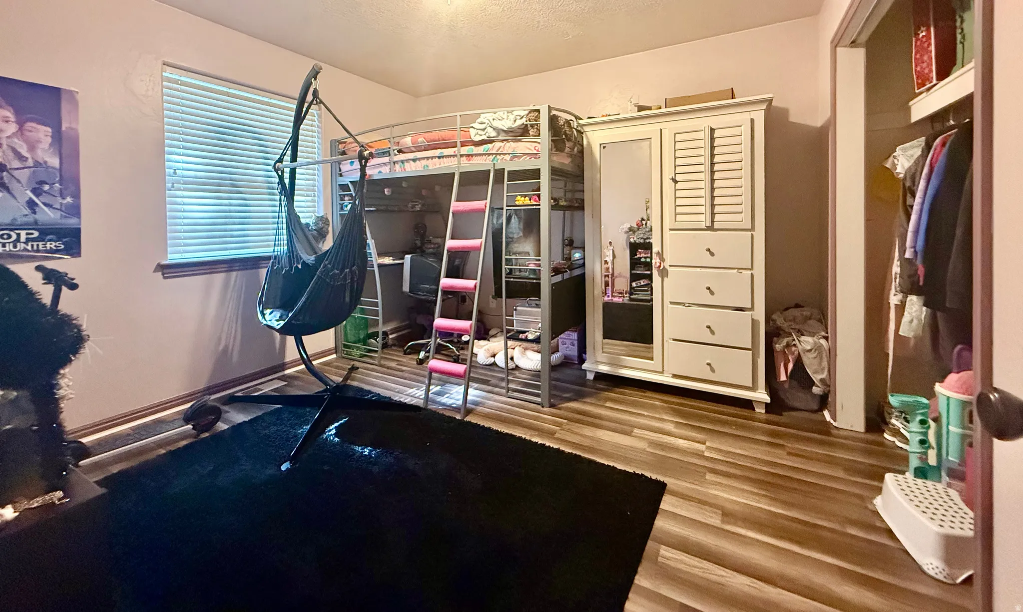 Room featuring wood-finish flooring, a metal loft bed frame with ladder, and a window with horizontal blinds