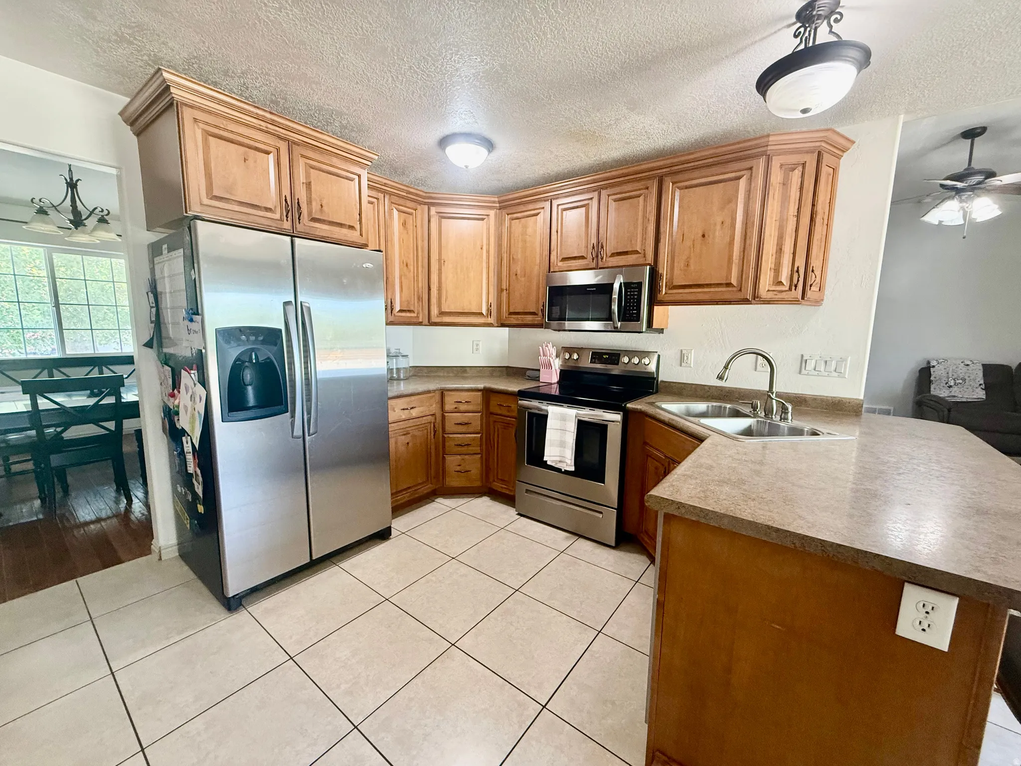 Kitchen featuring light wood cabinetry, stainless steel appliances, light tile flooring, a double basin sink with a high-arc faucet, and light countertops