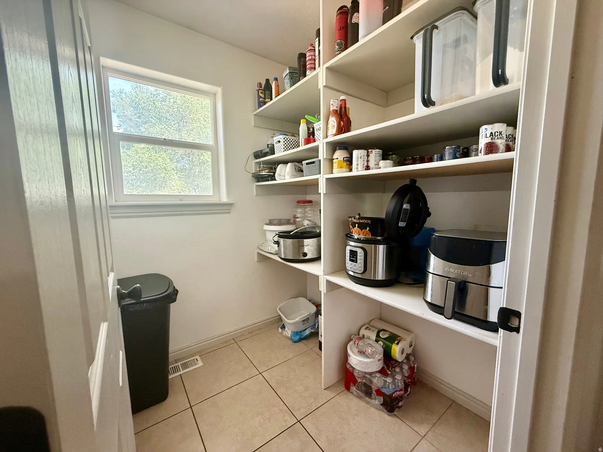 Spacious pantry featuring extensive built-in shelving, tile flooring, and a single window providing natural light