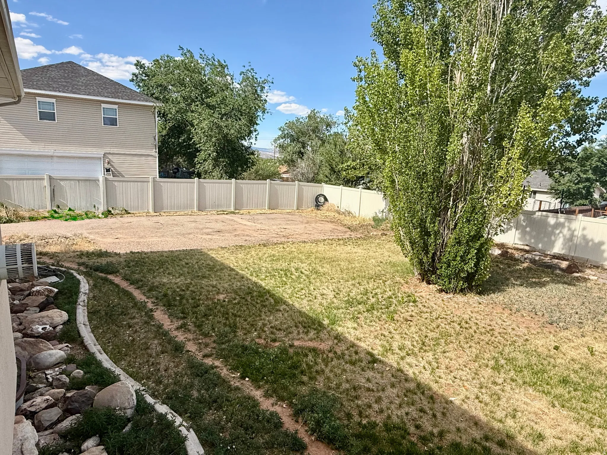 Expansive backyard featuring a large tree, perimeter fencing, a landscaped rock border, and an open area for customization