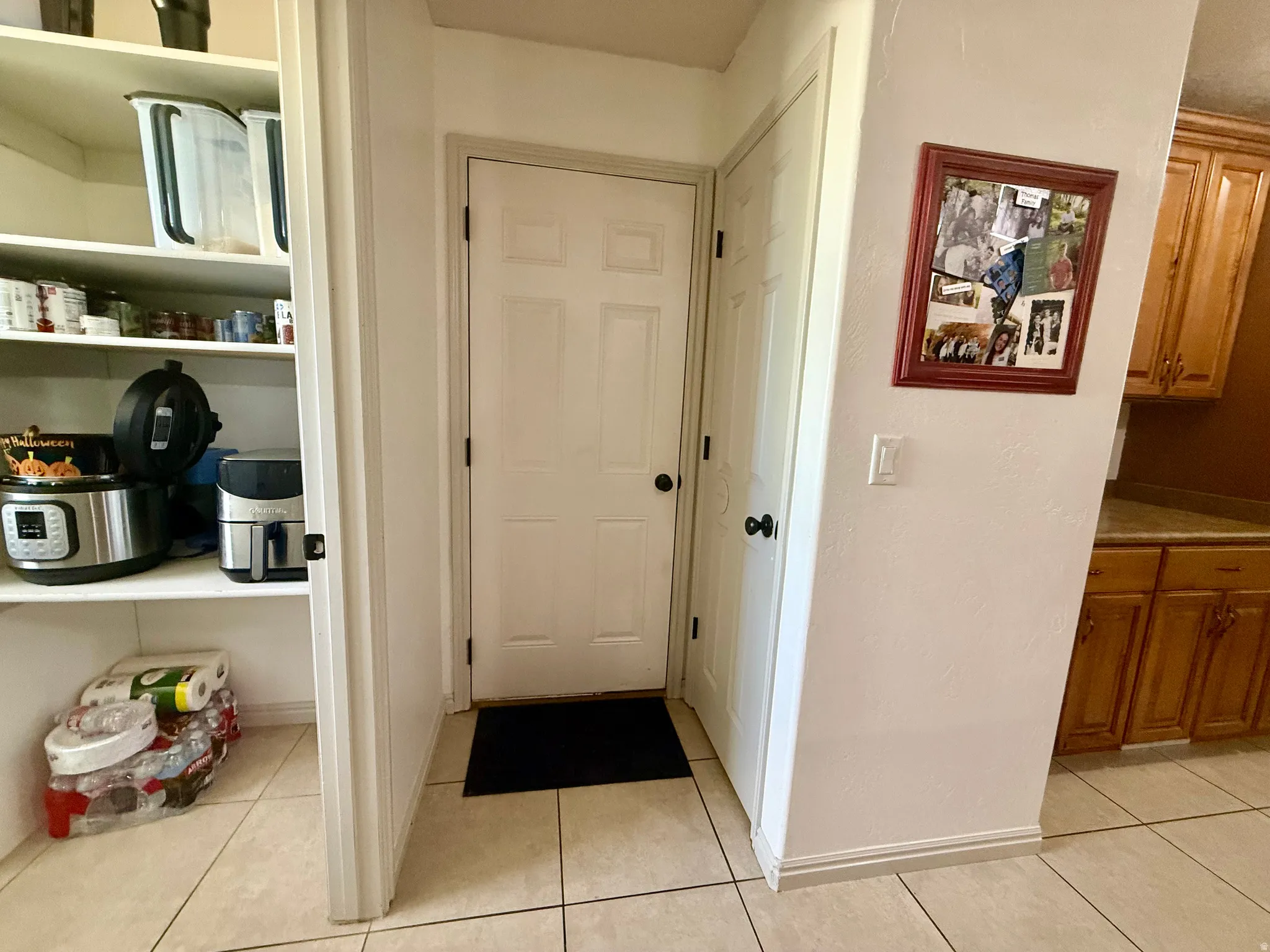 Pantry with built-in shelving, white paneled doors, and light-toned tile flooring