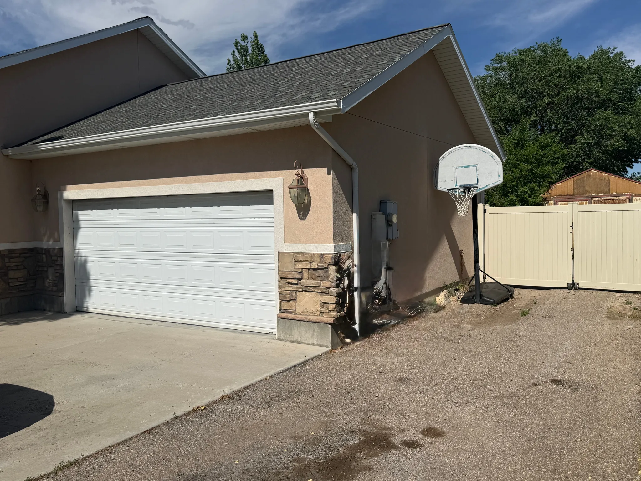 Attached two-car garage with a white sectional door, stone veneer detailing, and stucco exterior