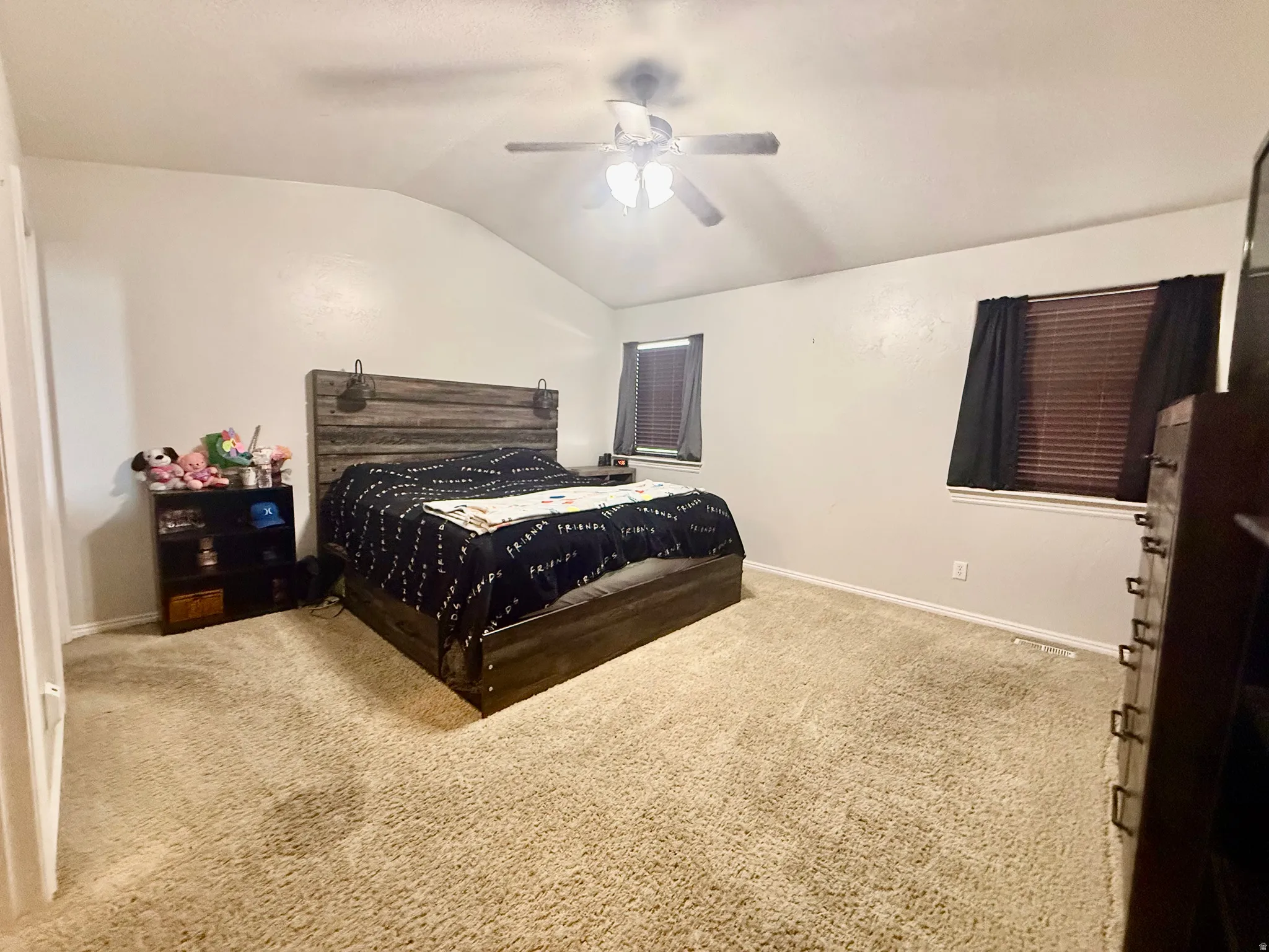 Spacious bedroom featuring light-colored carpet flooring, a vaulted ceiling, and a ceiling fan with integrated lighting