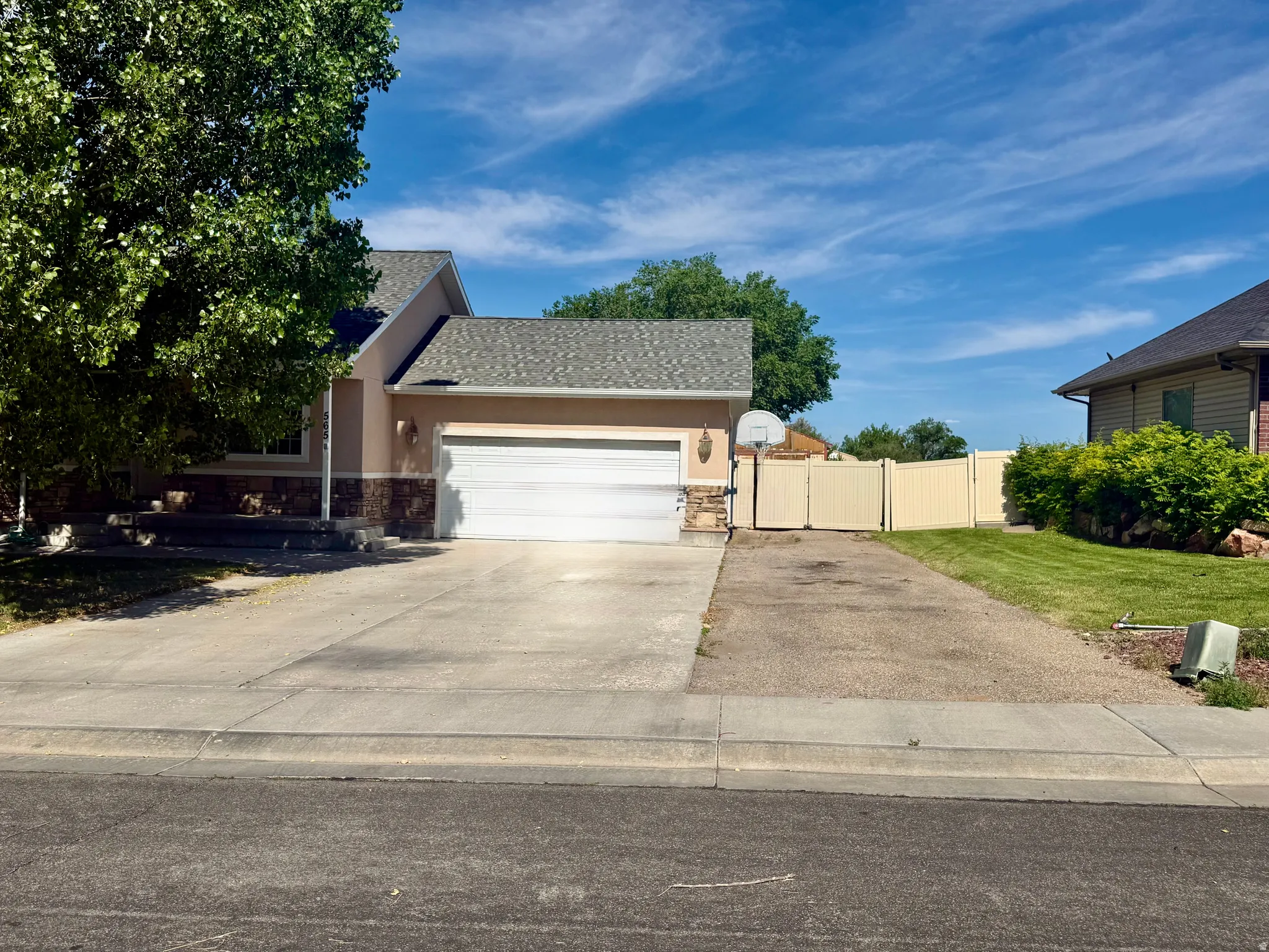 Exterior featuring a two-car garage, stone accent siding, a shingled roof, a paved driveway, and a light-colored privacy fence