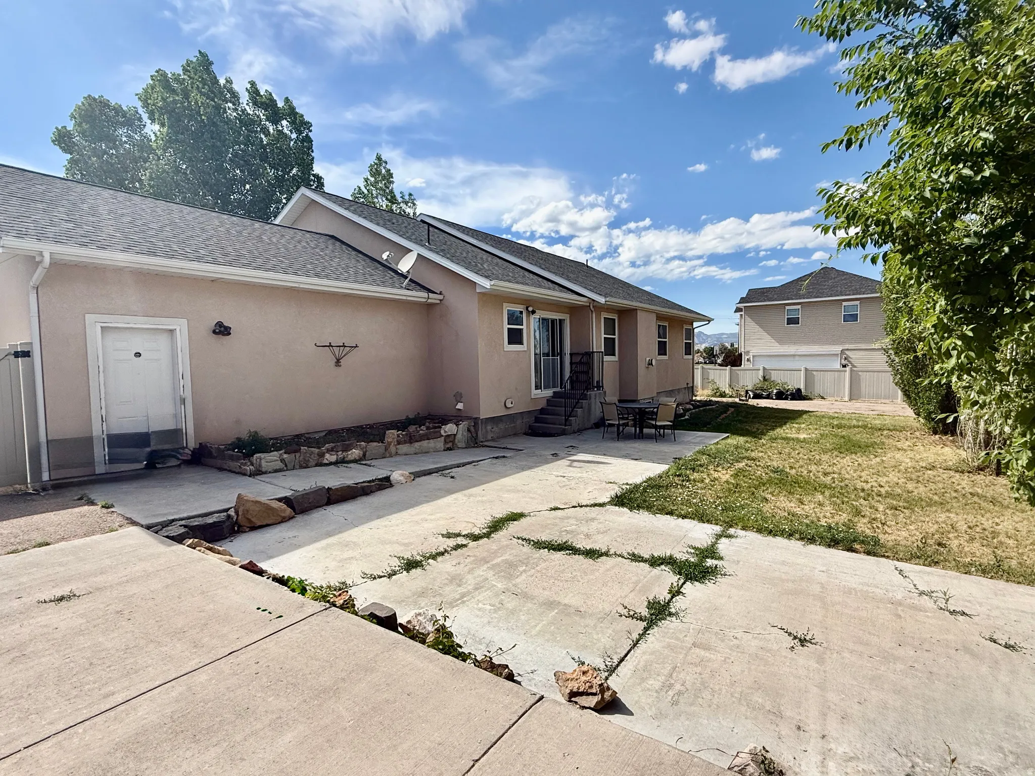 Rear exterior featuring light-toned stucco siding, a concrete patio area, and a grass lawn