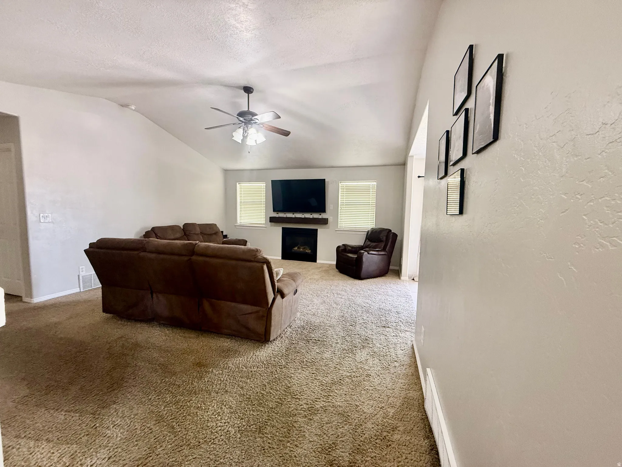 Spacious living area featuring vaulted ceilings, a ceiling fan with integrated lighting, and carpeted flooring