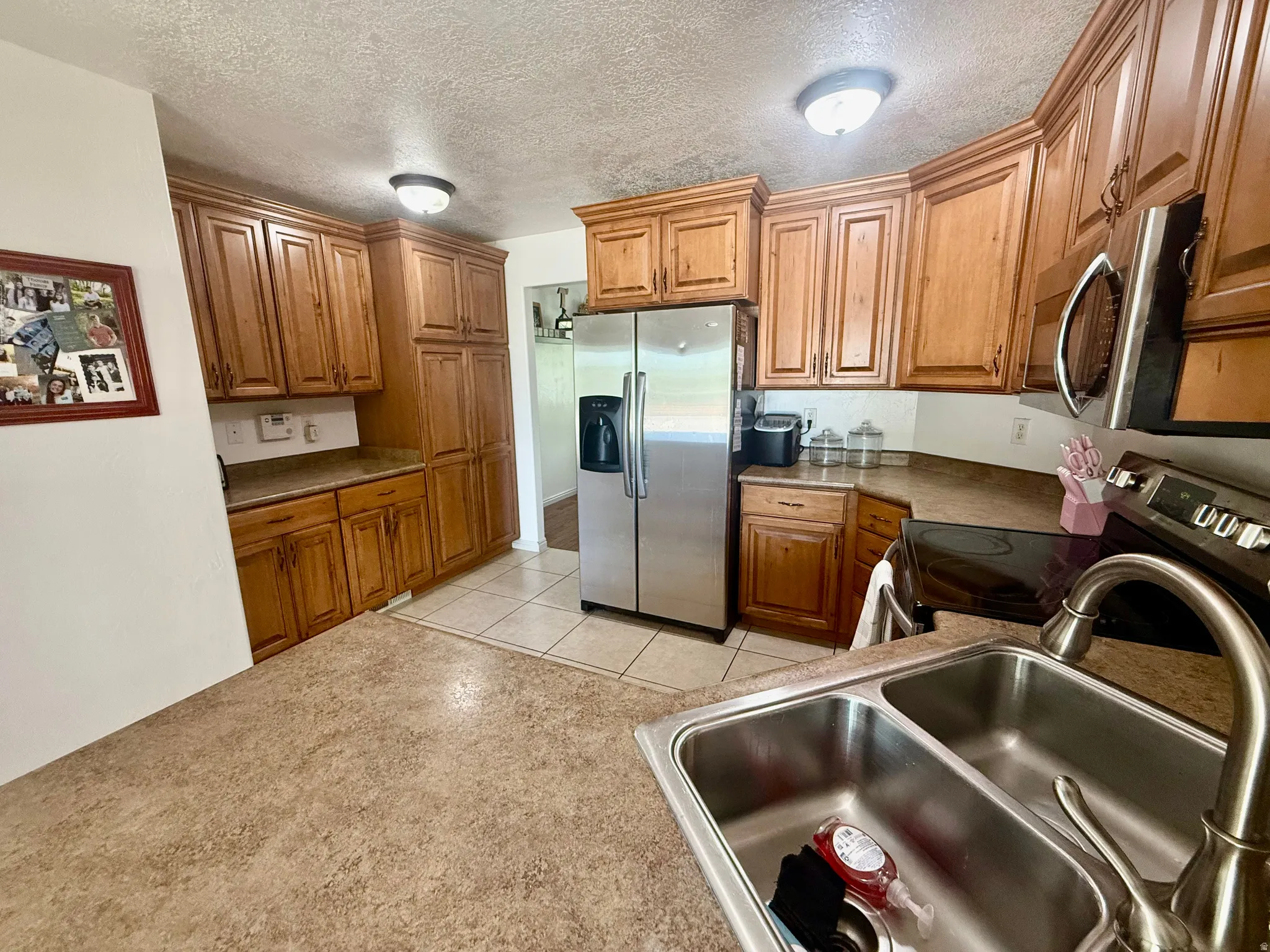Kitchen featuring wood cabinetry, stainless steel appliances, a double basin sink with a high-arc faucet, and tiled flooring